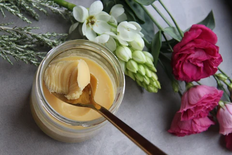 Grass fed butter in a glass jar with a serving spoon next to pretty pink and white flowers on top of a table to make weed bulletproof coffee