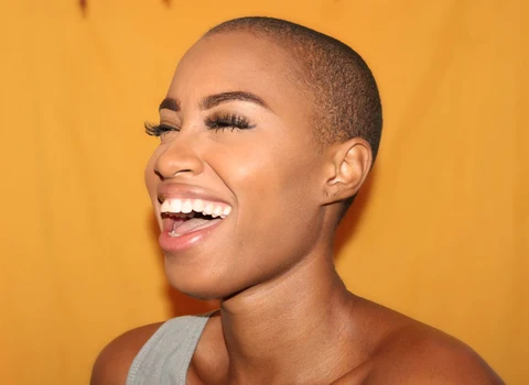 Ingesting is better than edibles: pic featuring a smiling black woman with a shaved hairstyle in a white shirt in front of a vibrant yellow background
